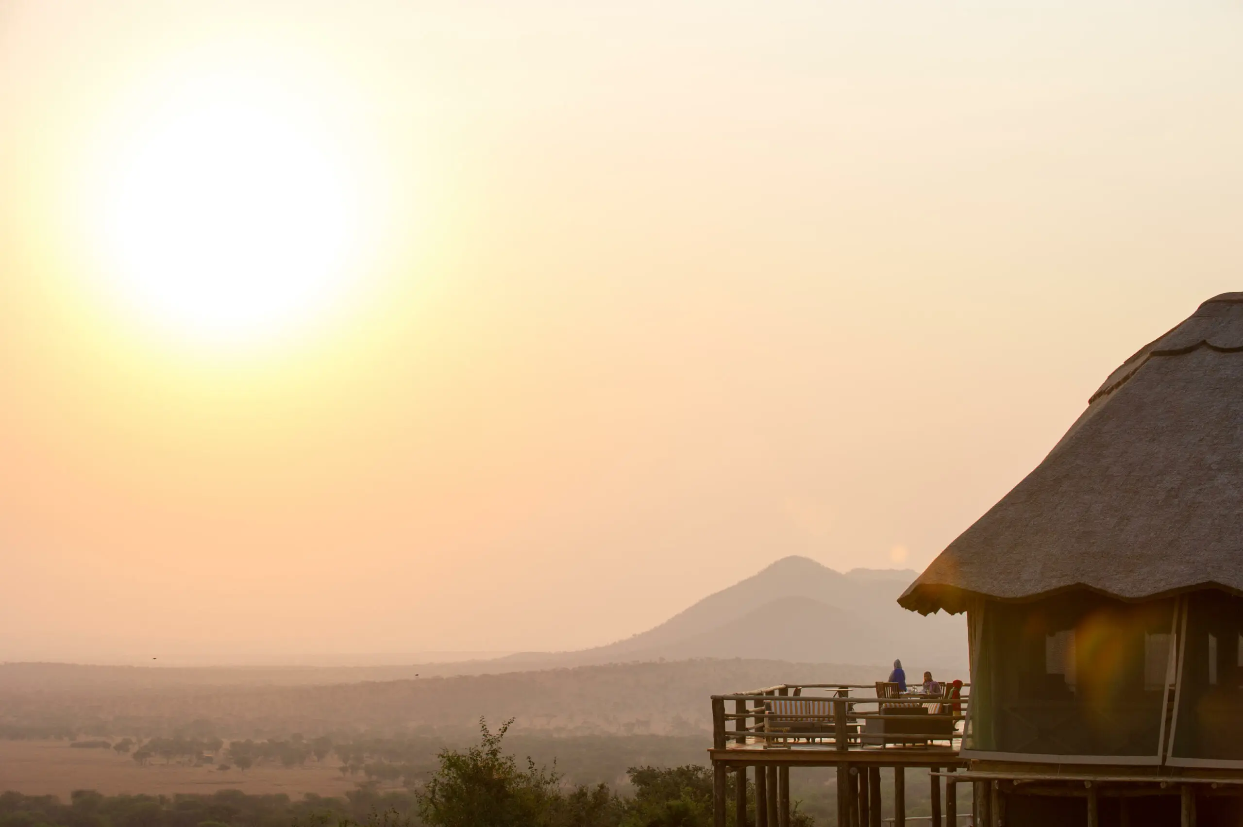 Couple on a safari lodge deck overlooking the Serengeti at golden hour